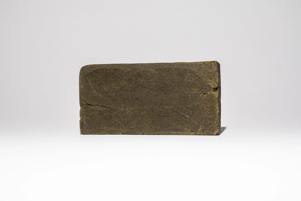 Single block of Afghan Charas 50% THCA hash on a light background, showing the smooth pressed surface and compact shape.
