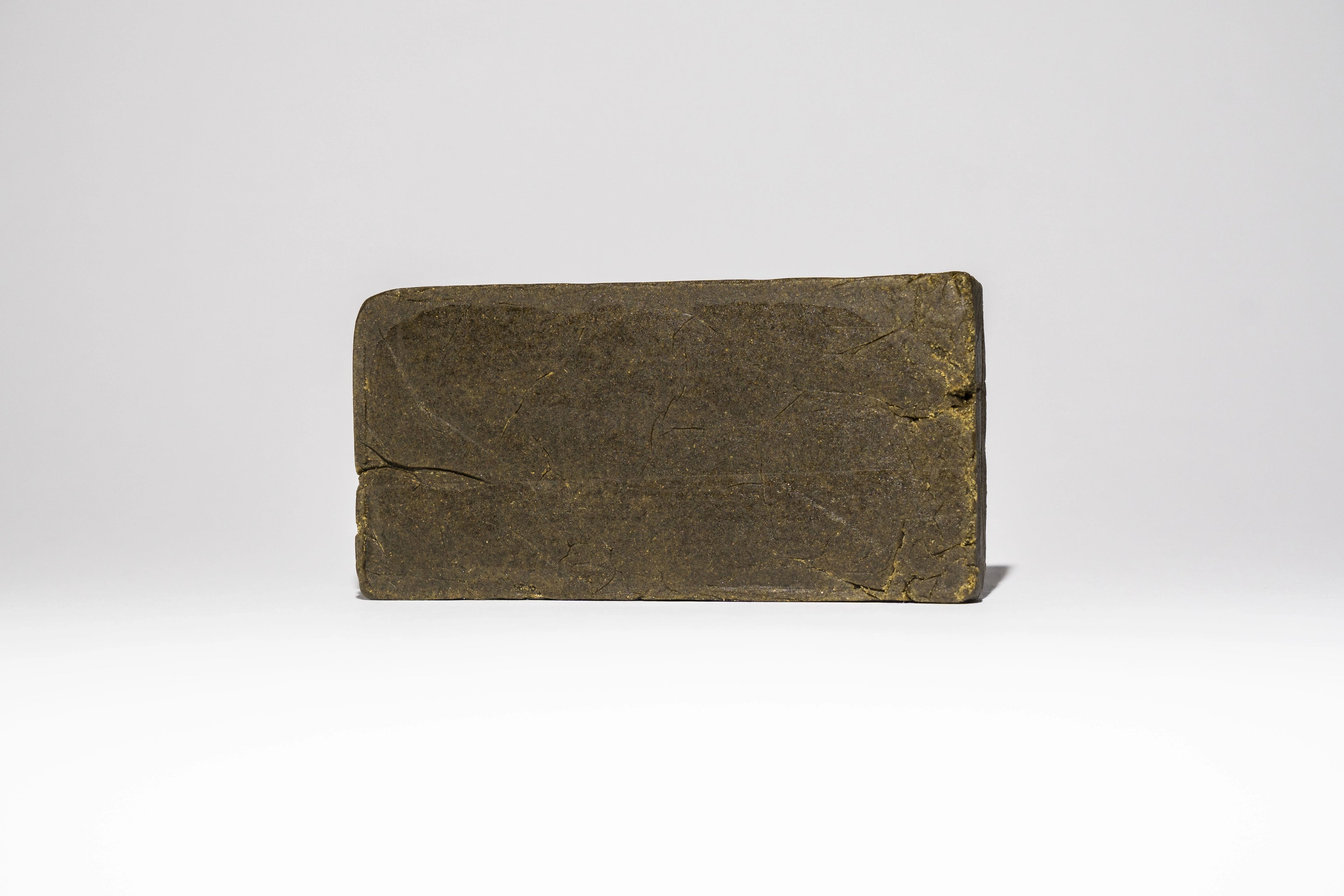 Single block of Afghan Charas 50% THCA hash on a light background, showing the smooth pressed surface and compact shape.
