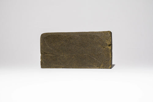 Single block of Afghan Charas 50% THCA hash on a light background, showing the smooth pressed surface and compact shape.
