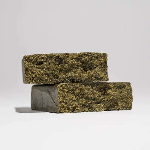 Two stacked pieces of Afghan Charas 50% THCA hash shown on a clean light background, highlighting the dense texture and pressed finish.
